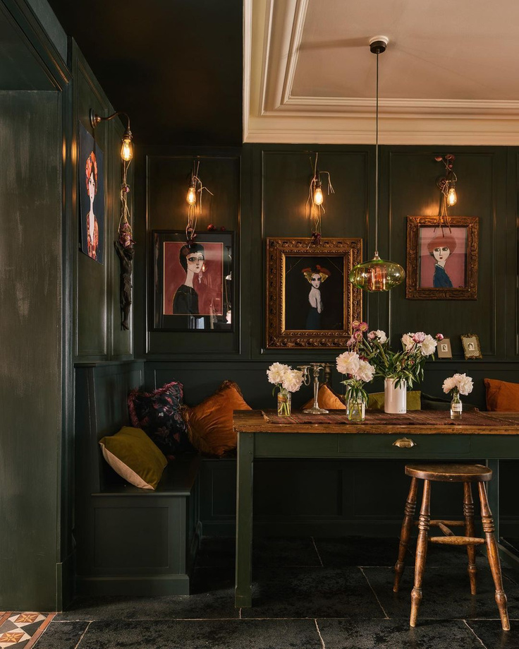 Moody dark green painted paneled walls and furniture in a kitchen dining area with industrial sconces and bespoke design - deVOL.