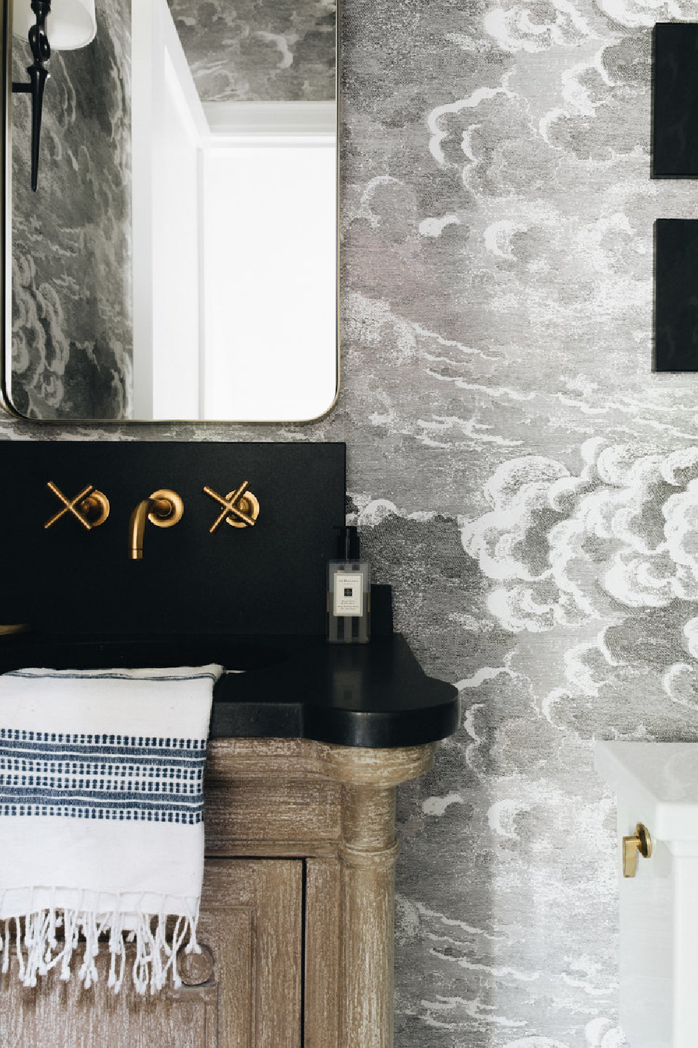 Atmospheric grisaille in a Kate Marker powder room with Fornasetti Nuvolette wallpaper.