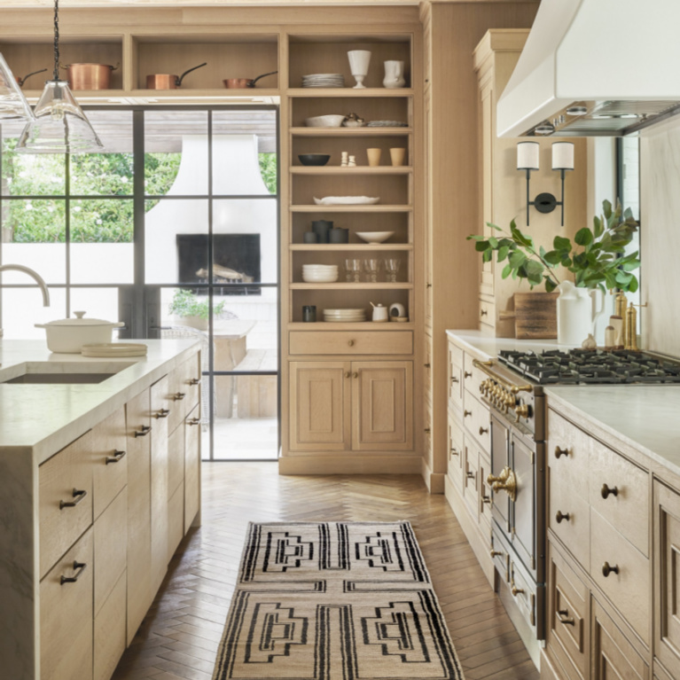 Modern rustic warmth in a kitchen with tone on tone light neutrals, herringbone wood floors, and luxurious range - Lulu & Georgia.