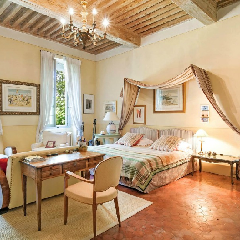 Elegant French country bedroom with sitting area in a Provence chateau with wood ceilings, yellow walls, and Old World built-ins - Haven In.