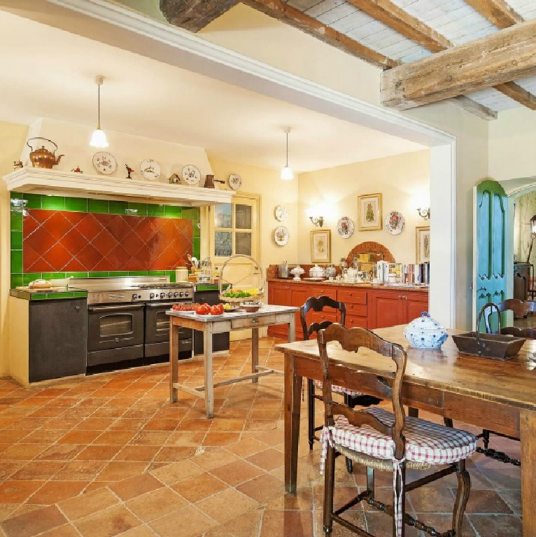 Cheerful and traditional with terracotta, green, and bright blue accents, this Provence kitchen with work table boasts timeless charm - Haven In. #frenchcountry #kitchens