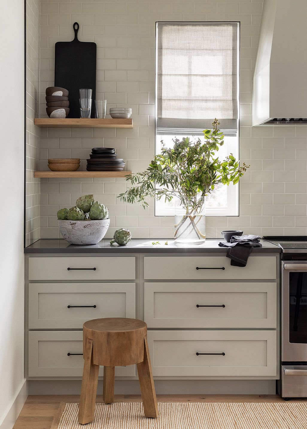 Rustic wood stool and floating shelves in a beautiful kitchen with design by Brian Paquette. #kitchendesign #floatingshelves