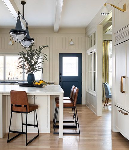 Leather counter stools in a gorgeous white kitchen with interior windows - design by Brian Paquette in AT HOME (Gibbs Smith, 2021). #kitchendesign #counterstools #coastalstyle