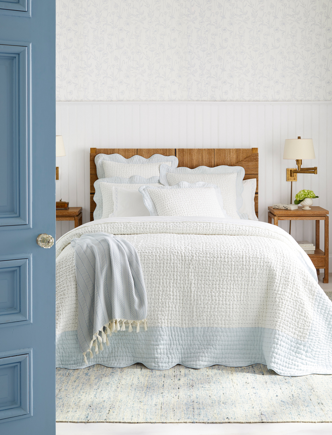 Coastal bedroom with classic blue painted vintage door and soft, airy, light and bright white quilt with light blue band - Serena & Lily.