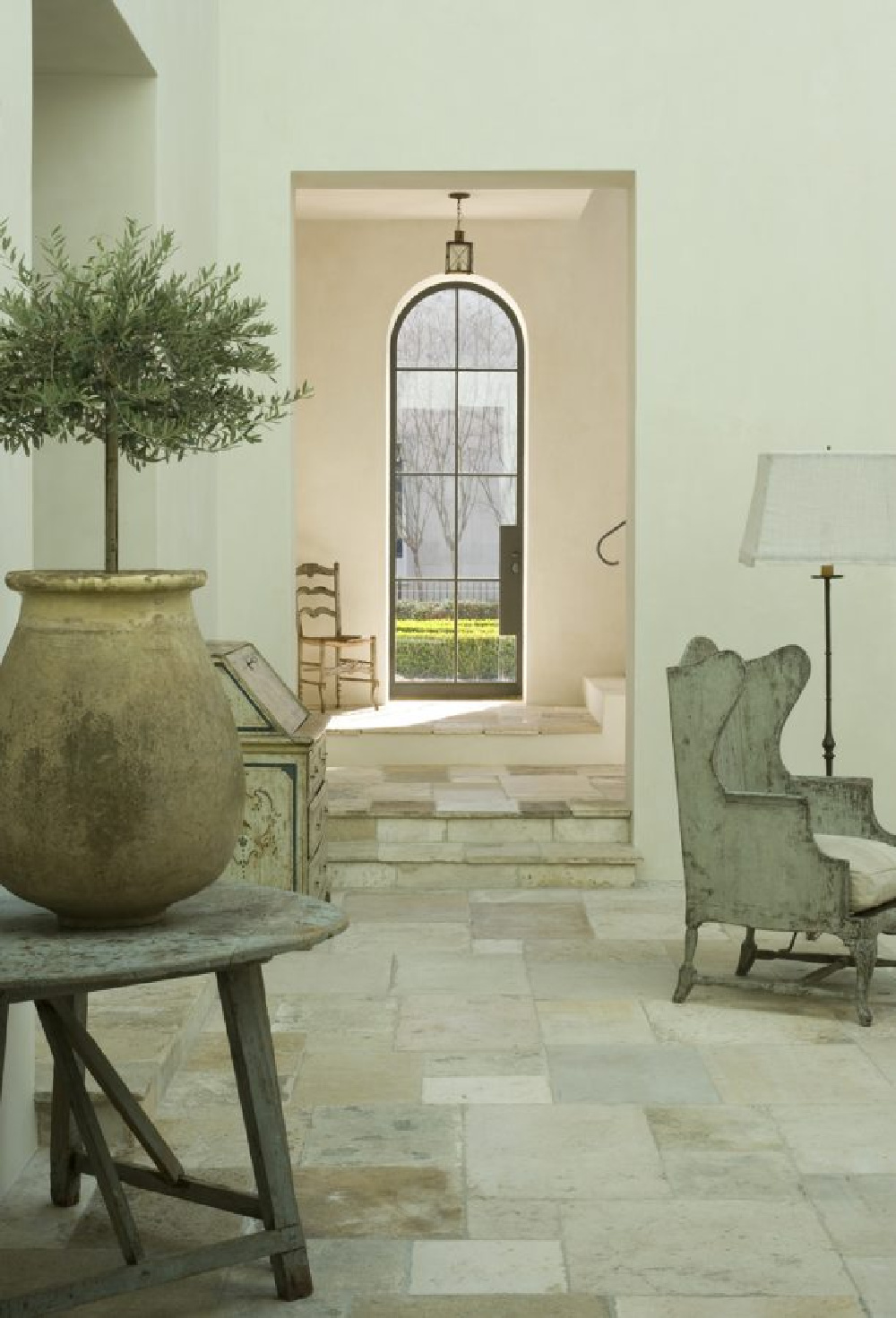 Hallway and family room with reclaimed stone flooring and arched steel door.  Come enjoy photos of this house tour with architecture by Reagan Andre.