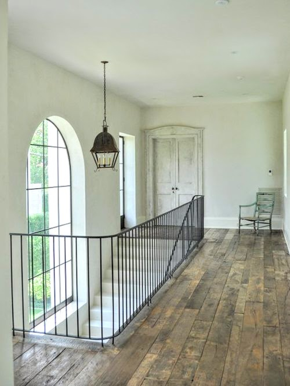 Luxurious mansion in Houston with rustic wood floors, lantern, and iron railing on stone staircase.