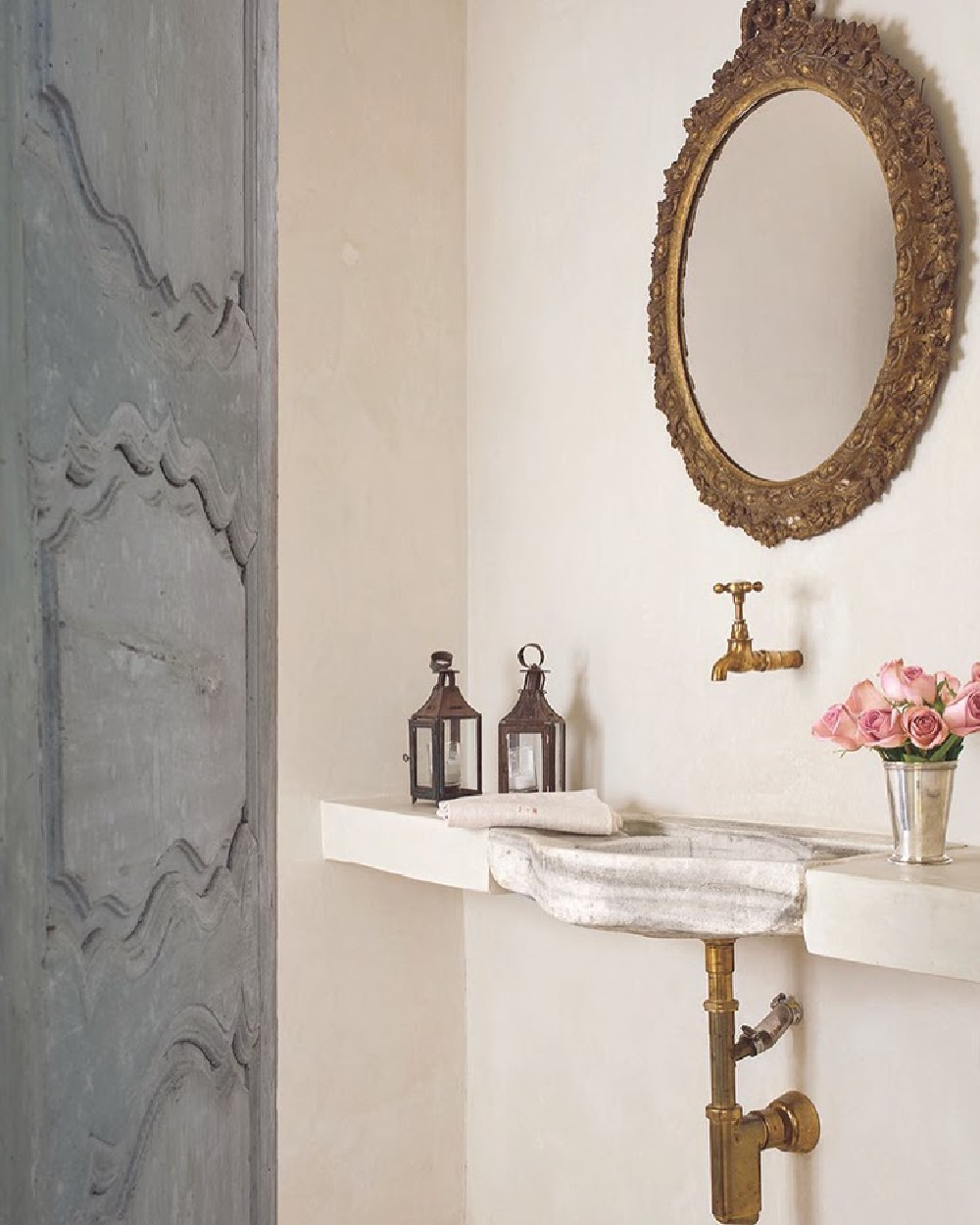 Luxurious and elegant powder room with blue antique doors, gilt mirror, and stone sink in Houston home with interior design by Pamela Pierce. Come enjoy photos of this house tour with architecture by Reagan Andre.