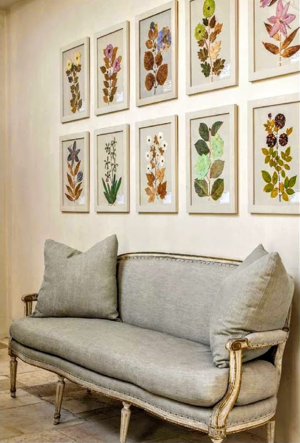 Vividly colorful framed botanicals hung above a French settee in an elegant home in Houston with interiors designed by Pamela Pierce.