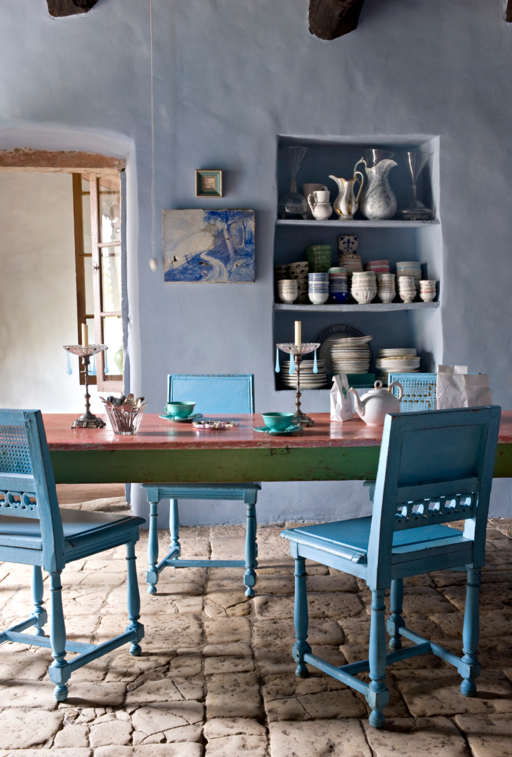 Blue grey plaster walls and bright French blue dining chairs play off each other in a charming monochromatic interior with rustic stone floor. Featured in Shauna Varvel's PROVENCE STYLE. #interiordesign #frenchcountry #oldworldstyle