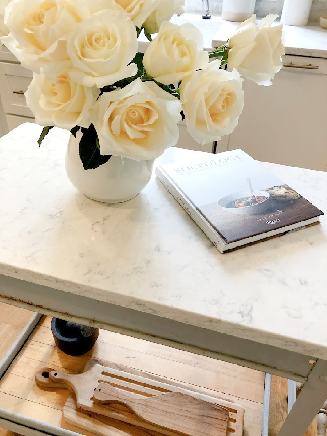 White roses in vintage ironstone pitcher on an industrial steel cart in my serene white kitchen - Hello Lovely. #whitekitchens #modernfrench #farmhousekitchen