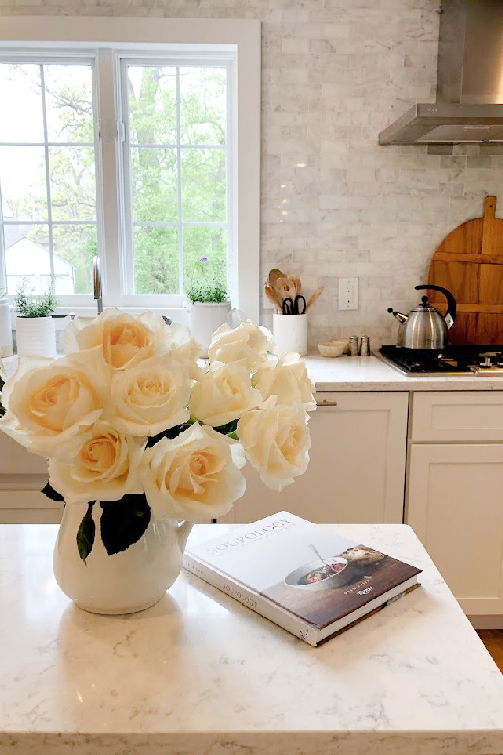 White roses in vintage ironstone pitcher on an industrial steel cart in my serene white kitchen - Hello Lovely. #whitekitchens #modernfrench #farmhousekitchen