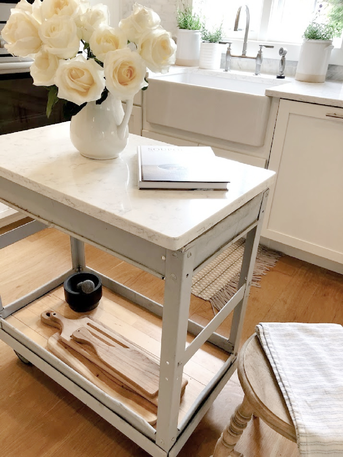 White roses in vintage ironstone pitcher on an industrial steel cart in my serene white kitchen - Hello Lovely. #whitekitchens #modernfrench #farmhousekitchen