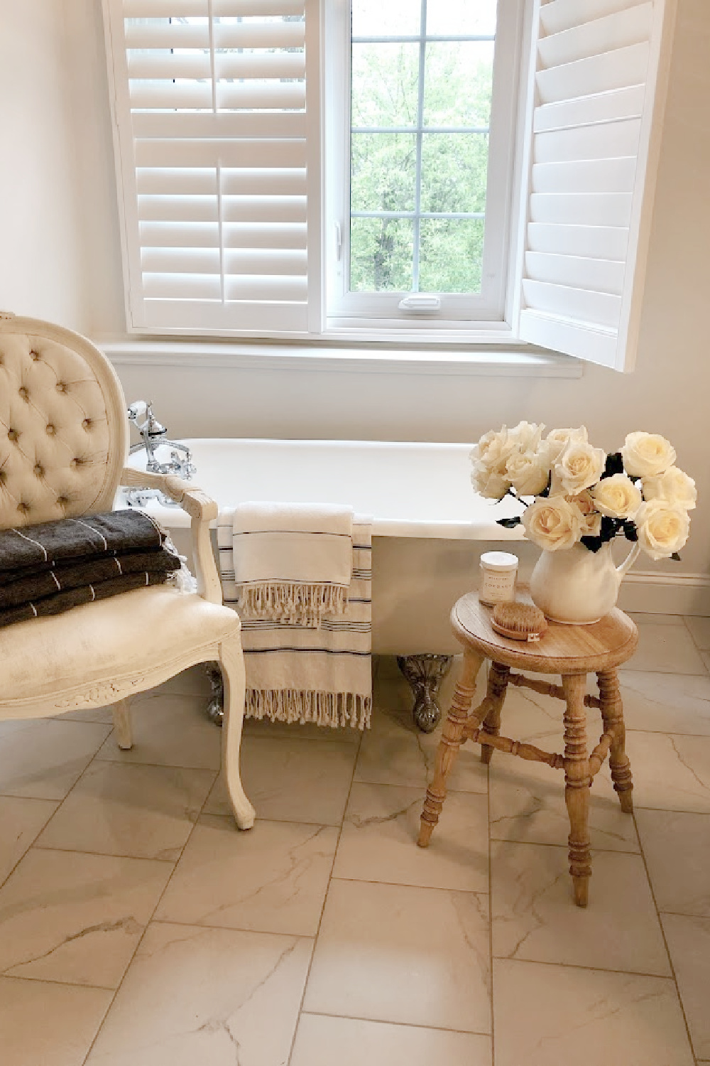 French country white bathroom with maids tub, accent stool, and white roses - Hello Lovely.