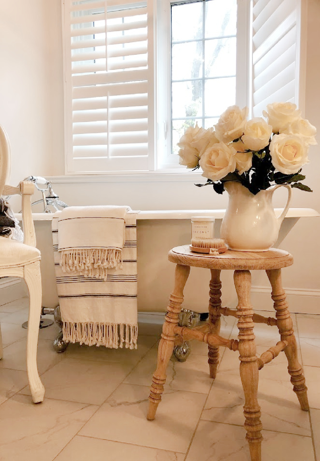 French country white bathroom with maids tub, accent stool, and white roses - Hello Lovely.