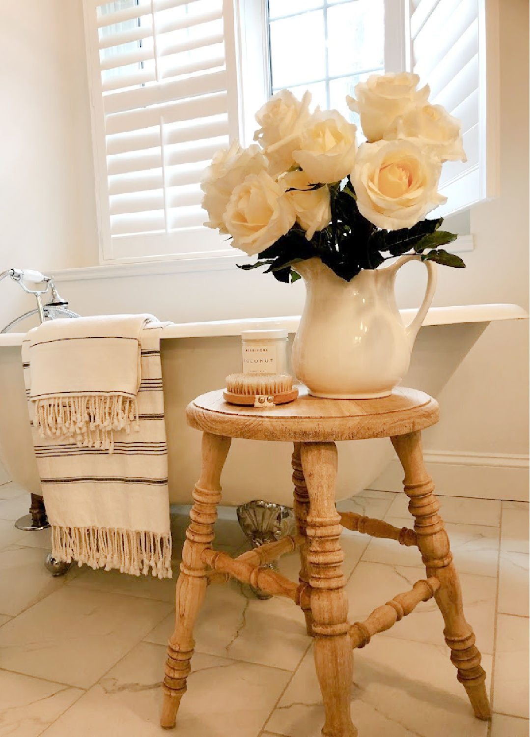 French country white bathroom with maids tub, accent stool, and white roses - Hello Lovely.