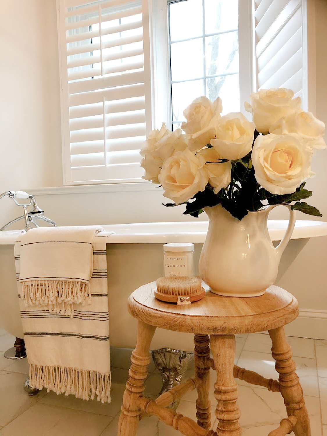 French country white bathroom with maids tub, accent stool, and white roses - Hello Lovely.