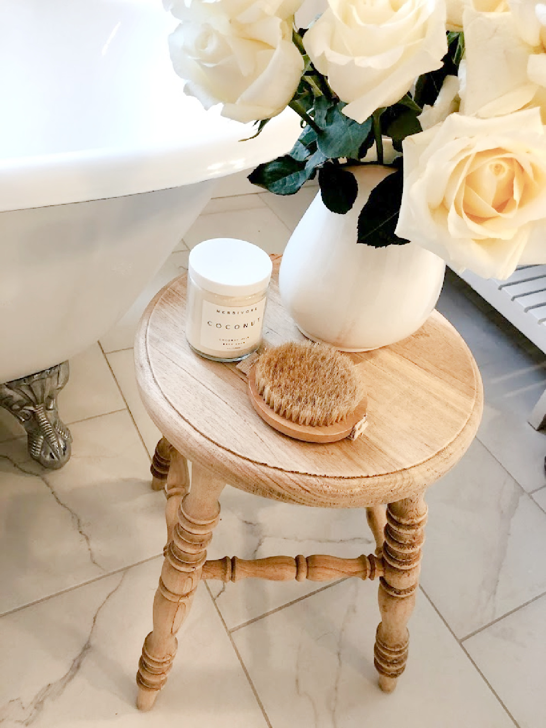 French country white bathroom with maids tub, accent stool, and white roses - Hello Lovely.