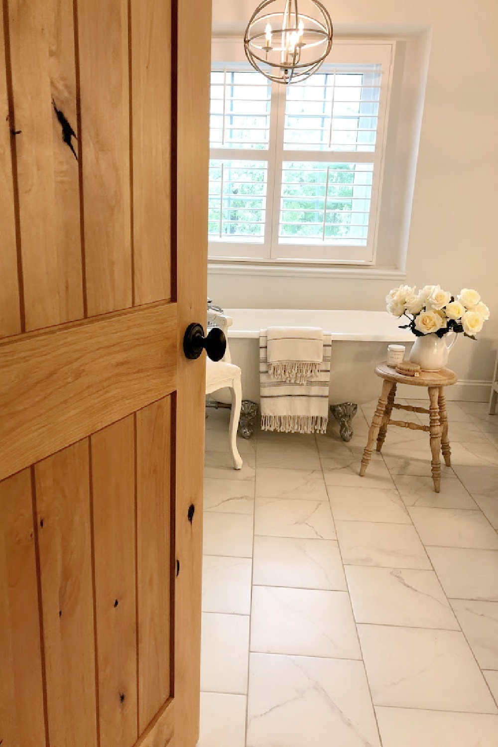 French country white bathroom with maids tub, accent stool, and white roses - Hello Lovely.