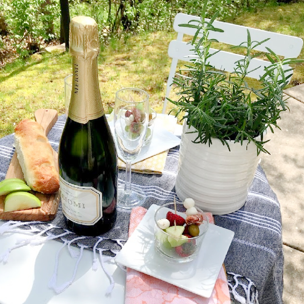 Champagne, French baguettes, and jarcuterie on a charming cafe table with rosemary centerpiece - Hello Lovely.