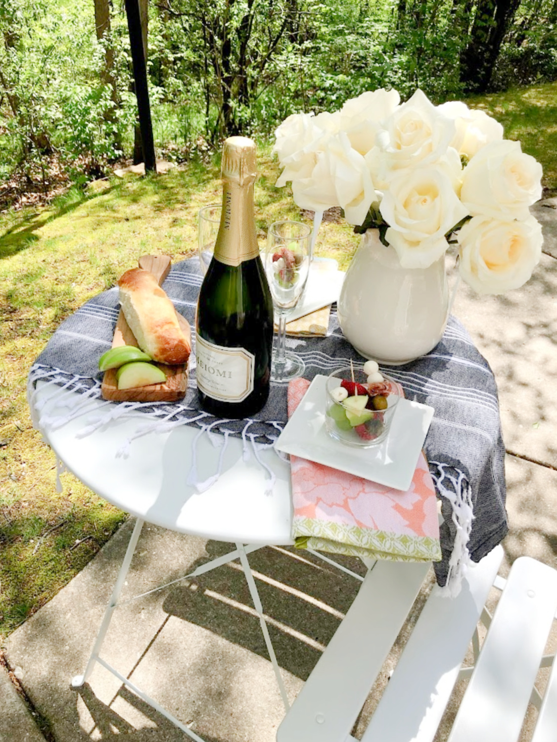 Petite French bistro table set with champagne, jarcuterie, and white roses - Hello Lovely Studio. #outdoordining #entertaining #frenchpicnic #jarcuterie