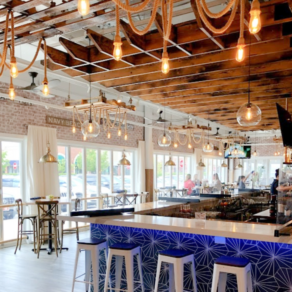 Nautical rope pendant lights illuminate the ceiilng and impart coastal vibes at The Hampton Social in South Barrington - Hello Lovely Studio. #coastaldesign #thehamptonsocial #hamptonstyle