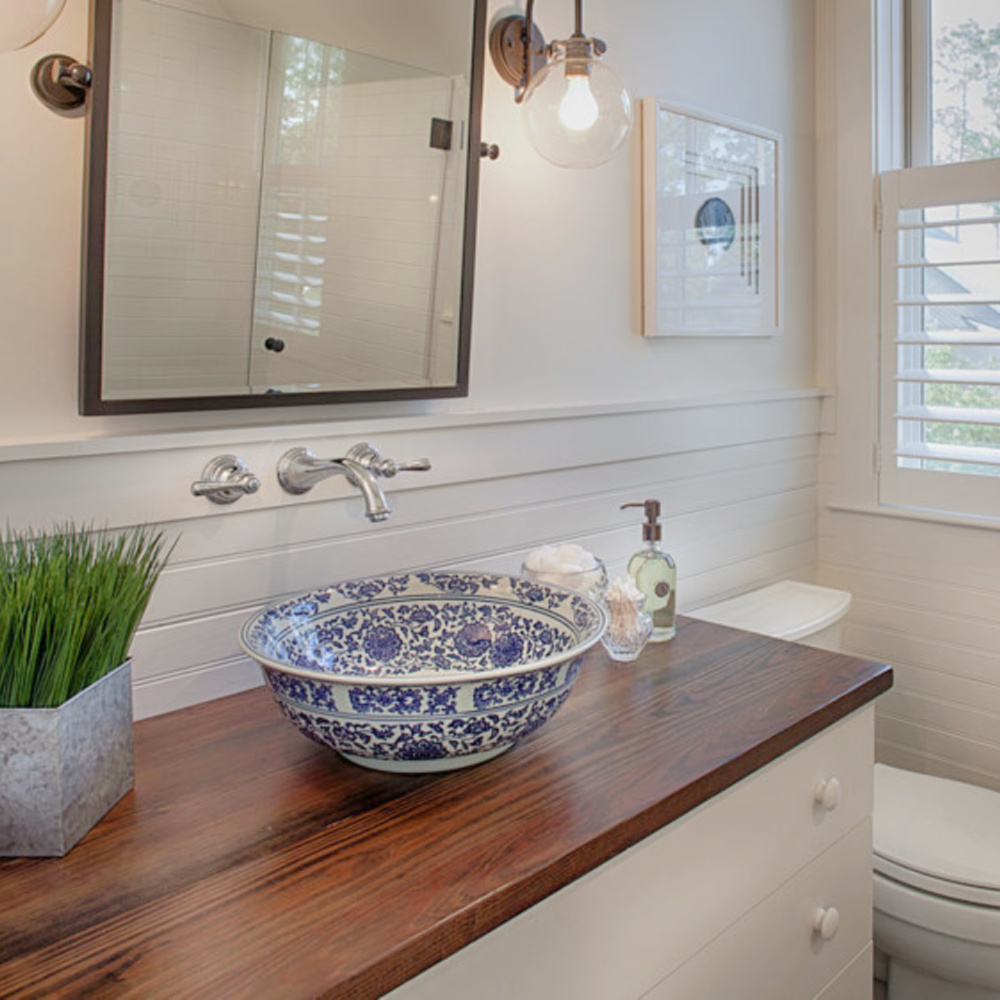 Blue and white vessel sink basin on a wood topped vanity in a coastal beathroom with wainscot and wall mount faucet. Design by Lisa Furey. #coastalstyle #bathroomdesign #vesselsink #blueandwhite #traditionalstyle