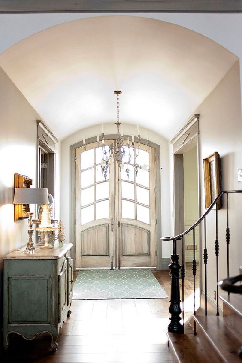 French Country style in a country home inspired by Europe. Heavenly sunshine floods the front entry hall of a French Nordic, French Country style hallway with barreled ceiling and blue grey stained trim.#frenchcountry #interiordesign #decorideas #entry #frontdoor #archeddoors #barrelceiling #staircase