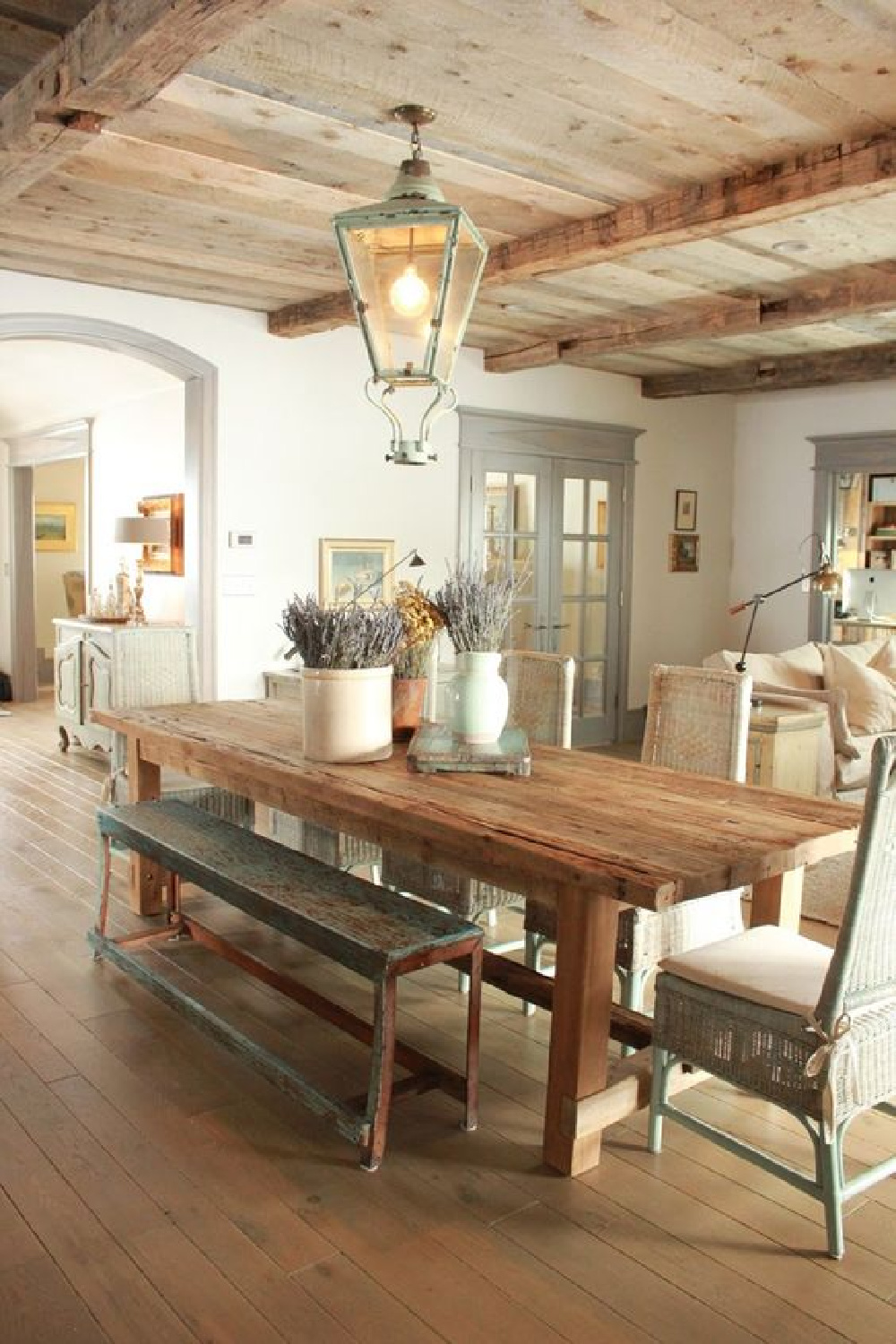 Rustic decor in a charming dining room with French farmhouse decor. Rustic farm table topped with stoneware holding lavender, knotty wood ceiling, vintage lantern, and blue grey trim throughout this home by Desiree Ashworth of Decor de Provence. Beautiful French Farmhouse Decor Images #frenchfarmhouse #vintagelantern #rusticdecor #diningroom #frenchcountry