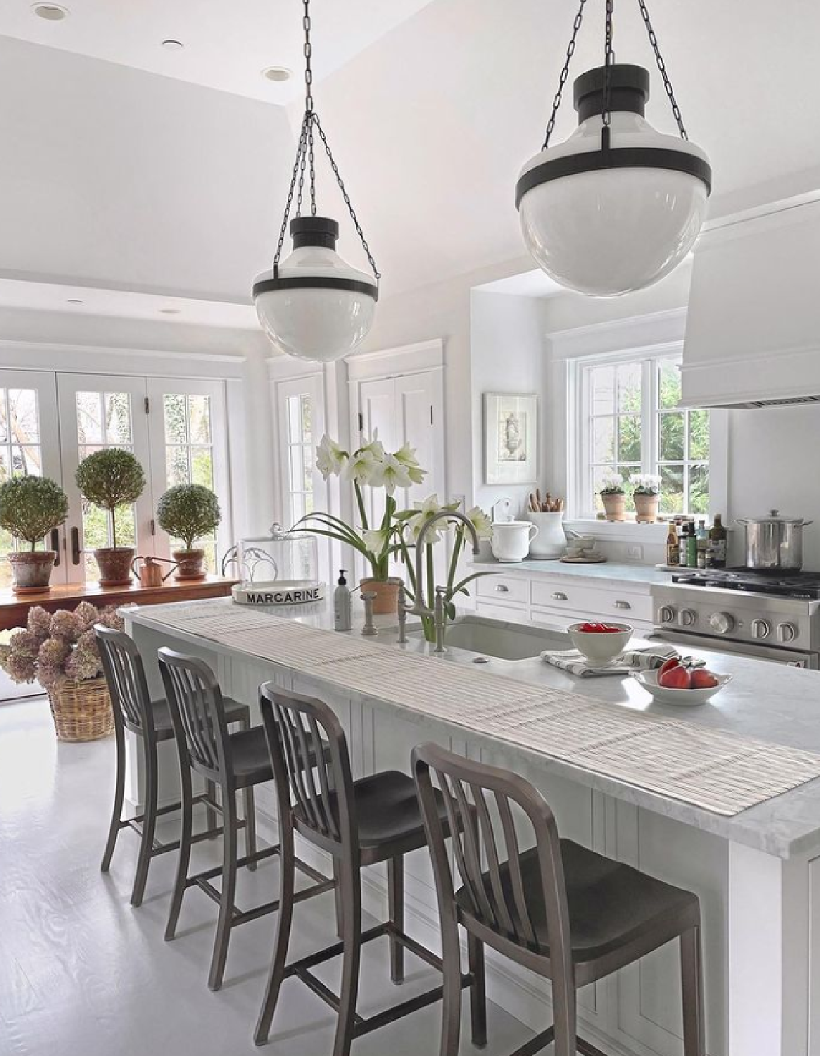 Chantilly Lace cabinets in a classic Nordic French white kitchen with light grey painted floors, topiaries near window, and classic pendants (Circa Lighting) over island - Loi of Tone on Tone. #whitekitchens #toneontone #bmshoreline #bmchantillylace