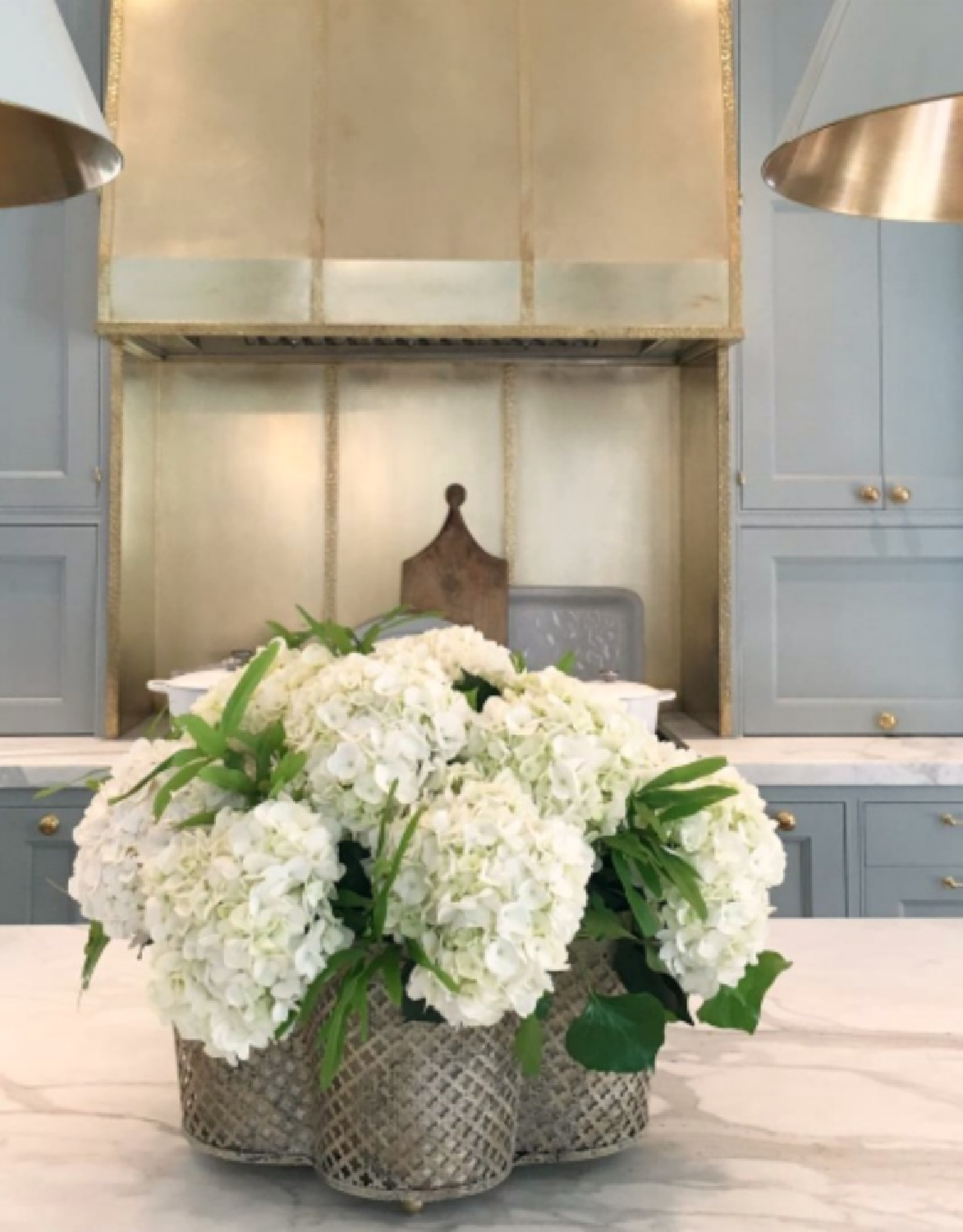 Farrow & Ball Light Blue painted cabinets, brass range hood, and white marble counters in Southeastern Designer Showhouse 2017 kitchen. #bluekitchens