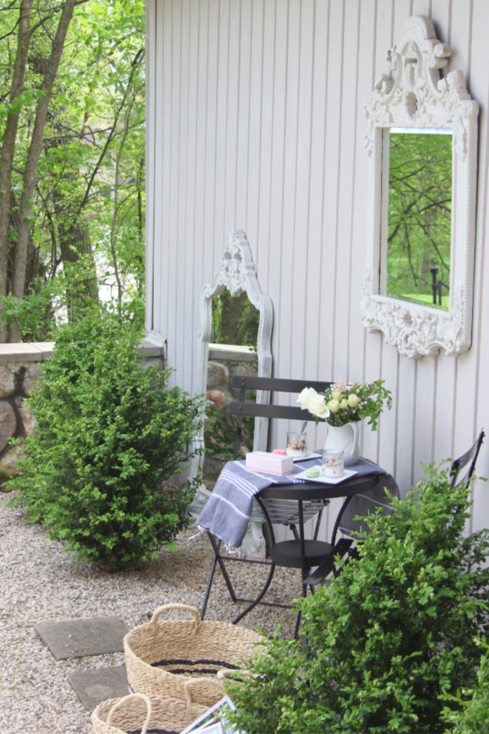 French country courtyard with boxwood, gravel, bisto set, baskets, and a French mirror. #hellolovelystudio #frenchcountry #bistroset #courtyard #gardendecor #boxwood #frenchbaskets #outdoordecor #outdooroasis