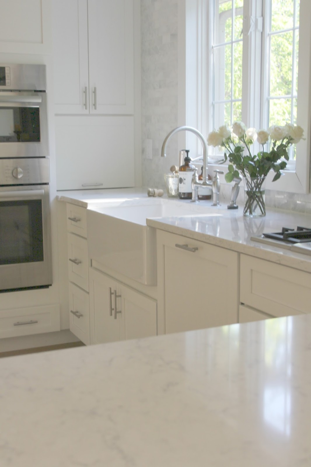 My white serene Shaker kitchen with farm sink, Bosch appliances, and Viatera (Minuet) quartz countertops - Hello Lovely Studio.