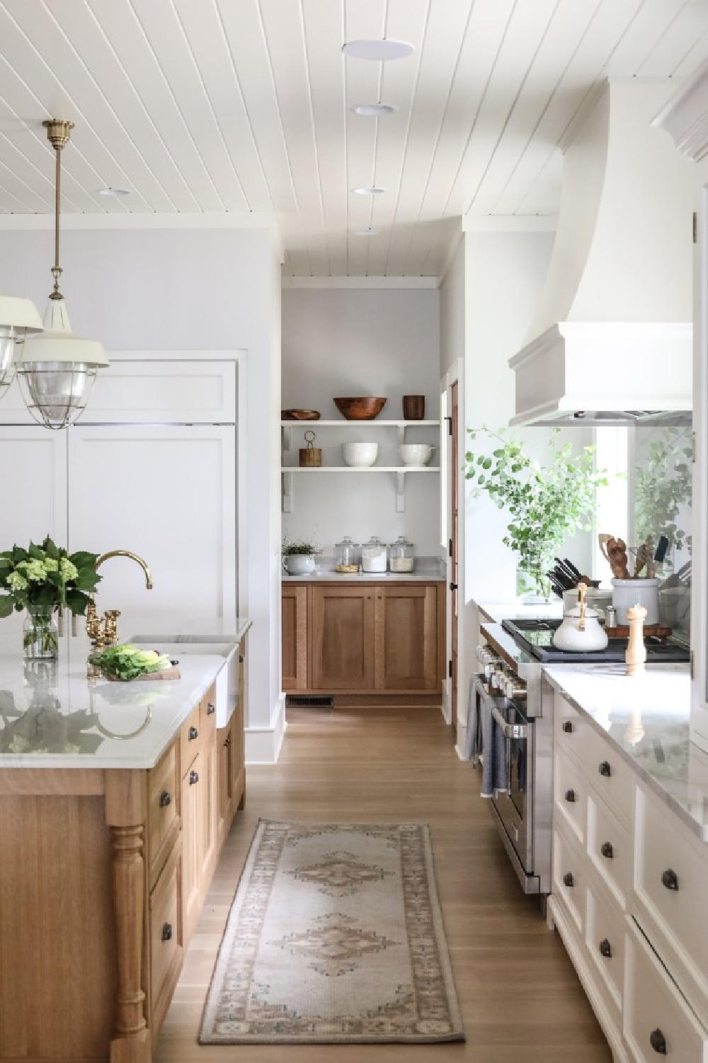 A magnificent timeless kitchen by Paark & Oak with wood stained island, coastal pendants, and white Shaker cabinets. Love the peek into the butler pantry! #whitekitchendesigns #classicwhitekitchen #traditionaldesign