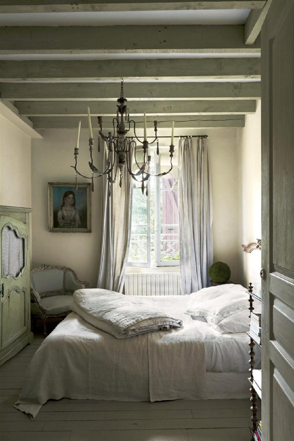 Ball Green by Farrow & Ball paint on the ceiling of a beautiful French country bedroom with chandelier and beams. #frenchcountry #frenchfarmhouse #interiordesign #farrowandball #ballgreen #paintcolors