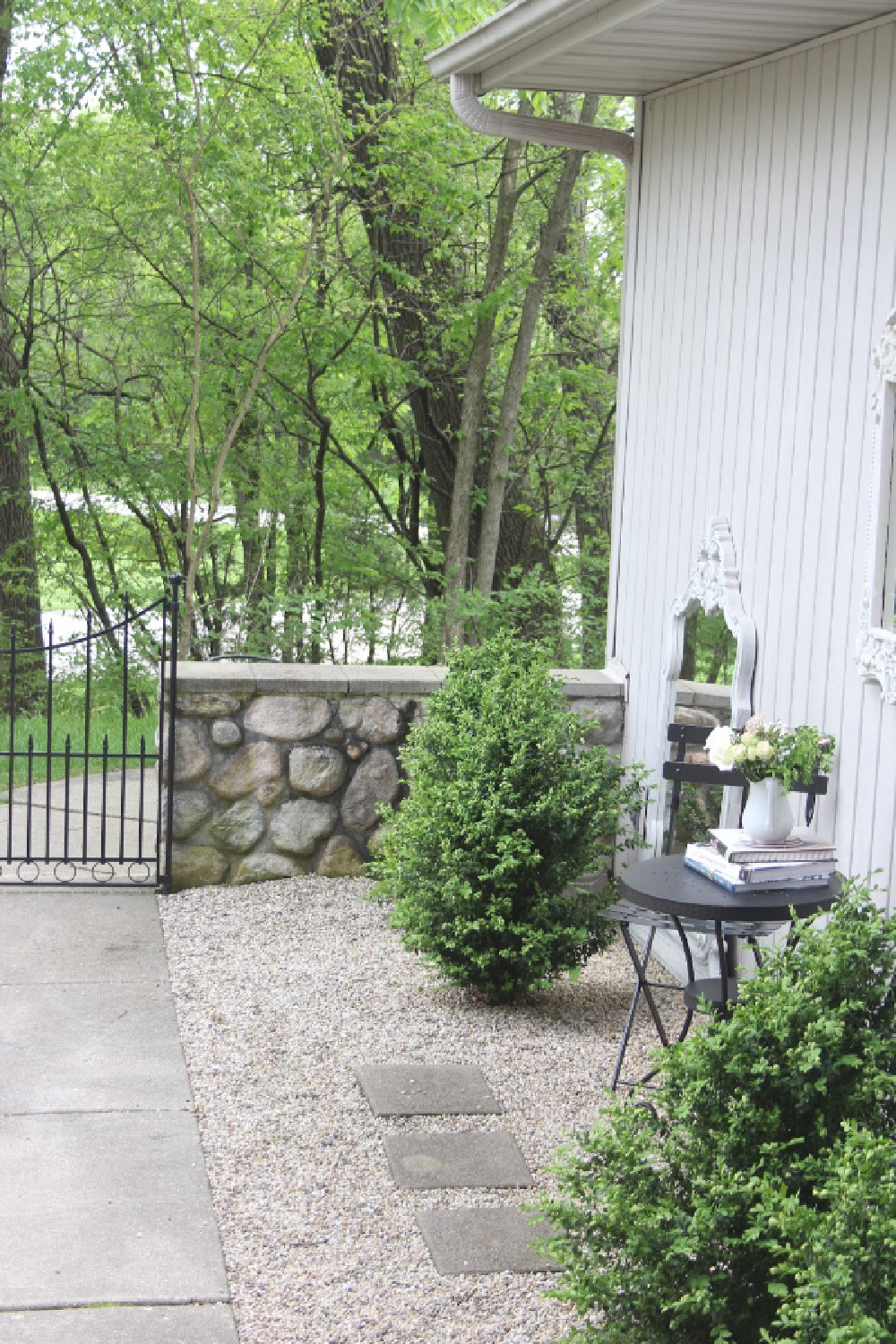 French country style courtyard with gravel and stonewall with a black modern French bistro dining area and boxwood. #hellolovelystudio #frenchcountry #modernfrench #courtyard #graden #outdoordining #outdooroasis