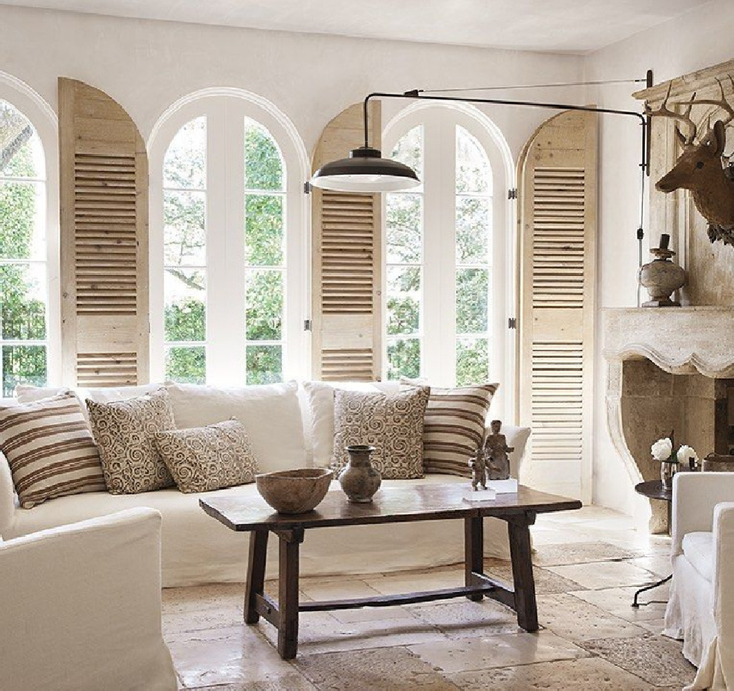 Pamela Pierce's Houston living room with arched windows, rustic shutters, and French limestone antique fireplace (Chateau Domingue). #rusticelegance #livingrooms #rusticFrenchinteriors