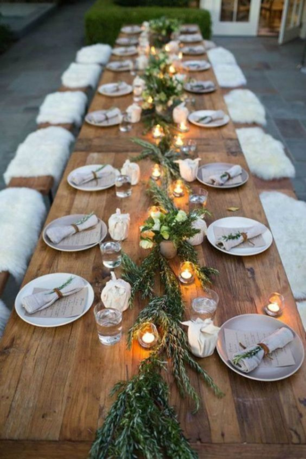 Rustic outdoor fall tablescape with long farm table, candlelight, and sheepskin over benches - Williams Sonoma. #falltablescape #farmhousefall #outdoorentertaining