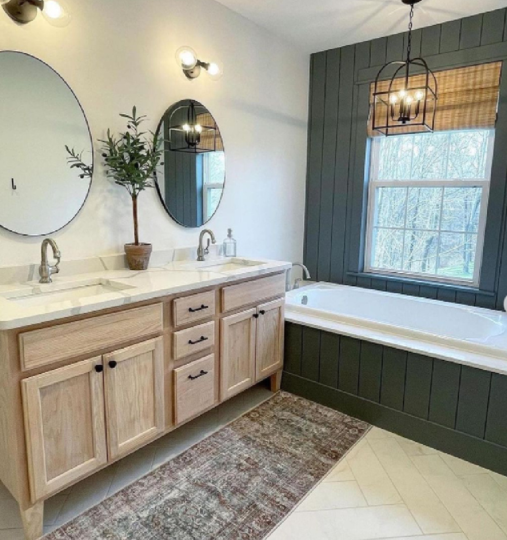 Remodeled bathroom with light wood vanity, round mirrors, and dark accent tub wall. (Before_and_After_Houses)