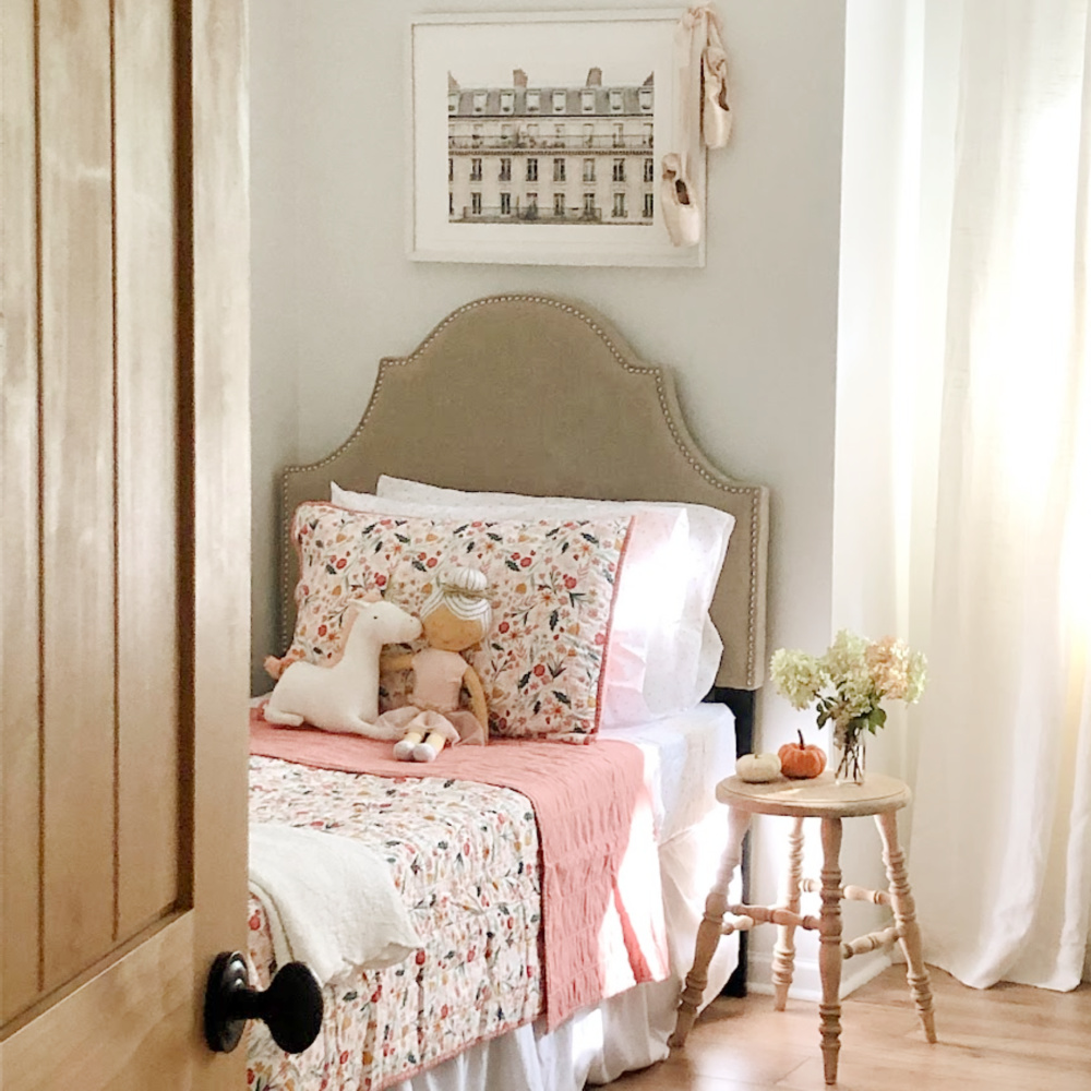 Hello Lovely's sweet girls bedroom with floral quilt, farmhouse stool as table and rustic alder door.