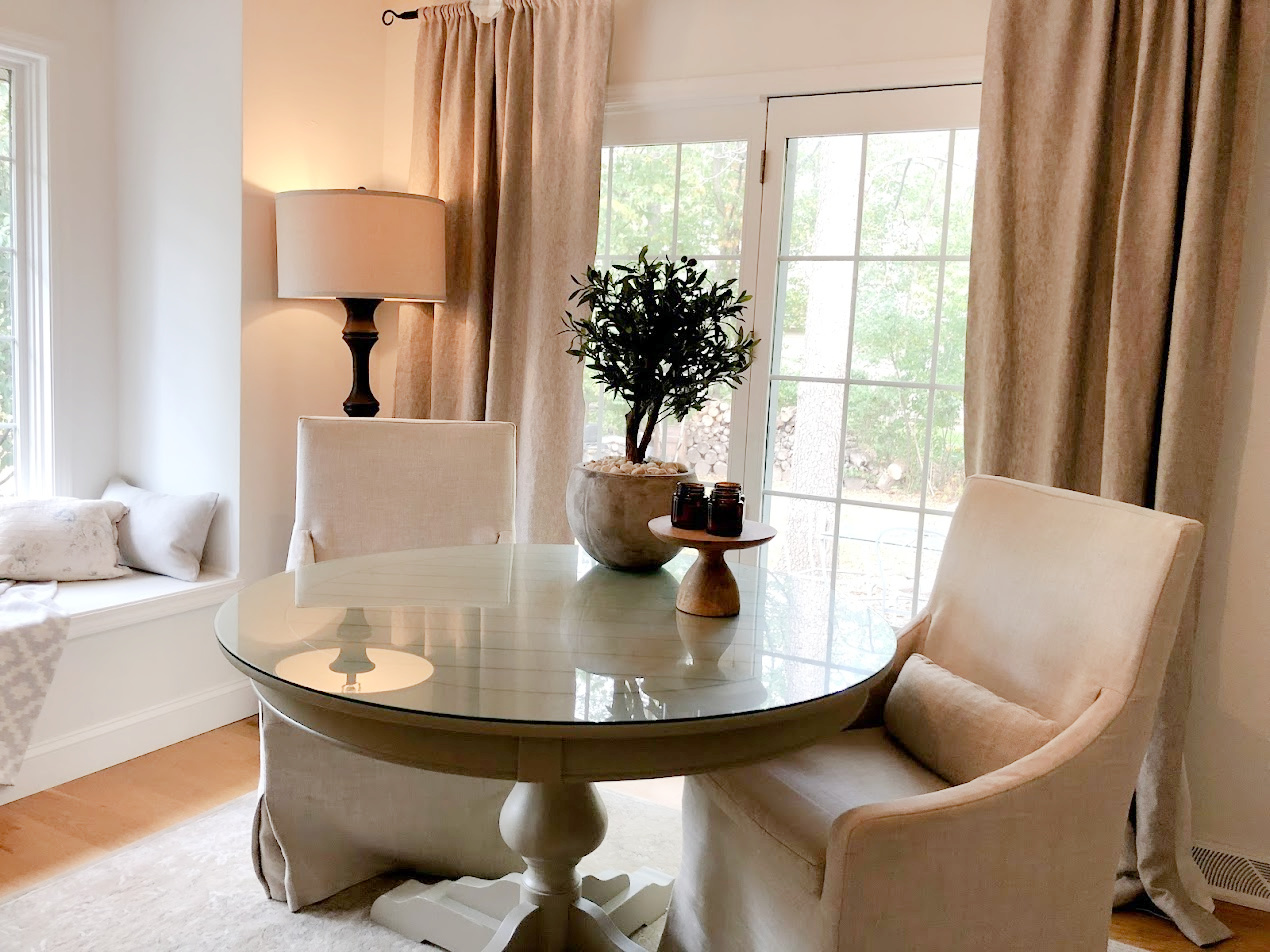 Serene breakfast nook with linen slipcovered chairs and round dining table - Hello Lovely Studio.