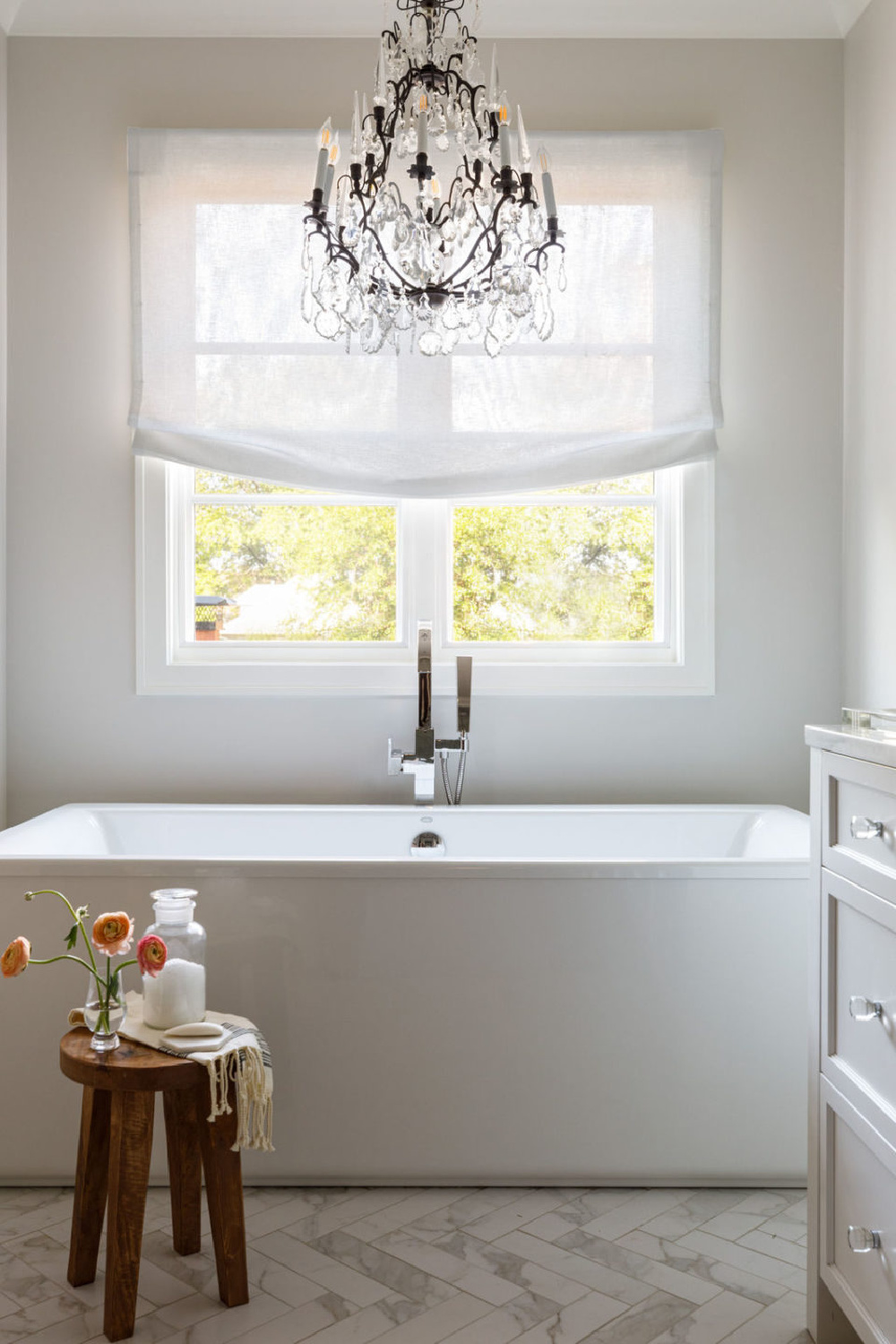 Serene and timeless white bath with soaking tub, crystal chandelier, and linen shade - design by Michael Del Piero.