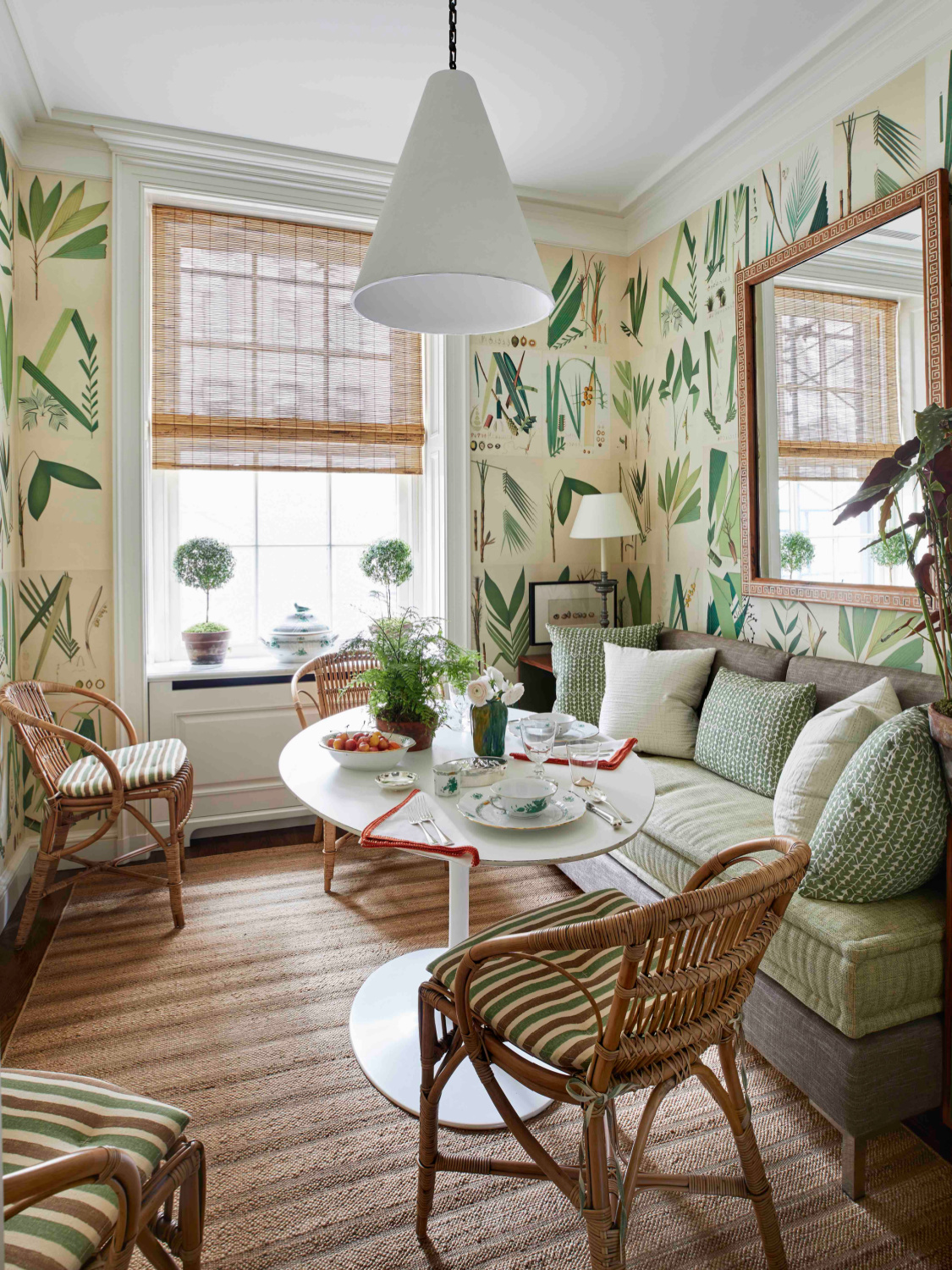 Cheerful green breakfast room designed by Tom Scheerer with sofa, oval tulip table, bamboo chairs, and walls papered in 1890s botanical prints by Joao Barbosa Rodrigues. #timelessdesign #greenwallpaper #tomscheerer