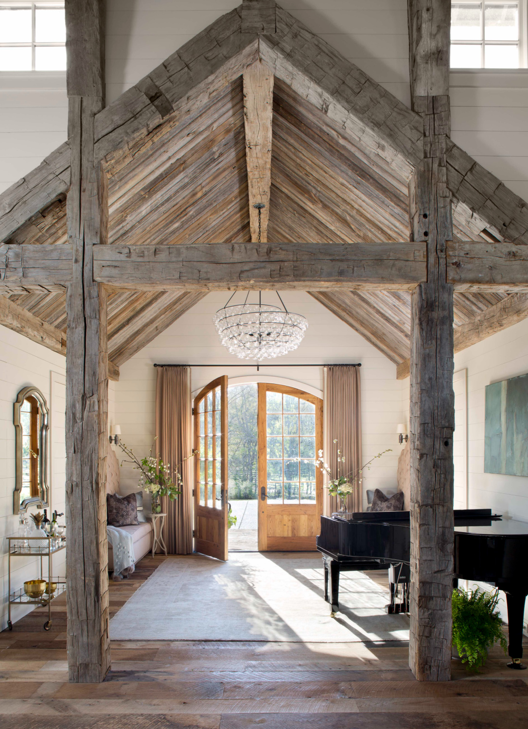 Dramatic entry with antique ceiling beams and arched custom front doors with glass in home by architect Brad Norris. #timelessdesign #rusticarchitecture #sticksandstones #bespokehomes