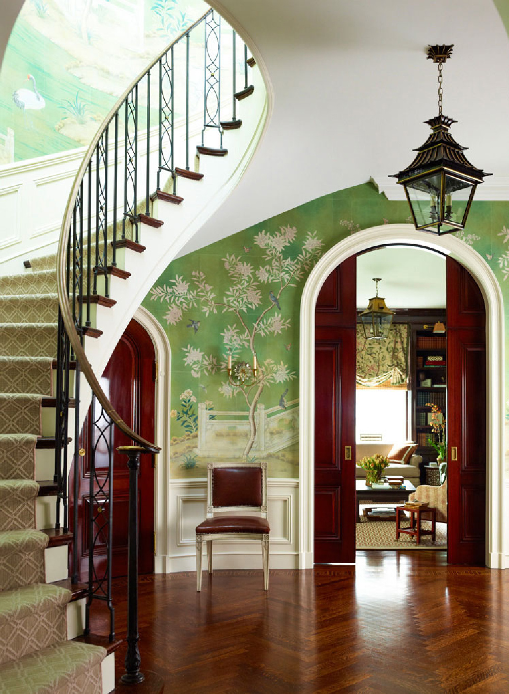 Green plays a starring role in this Ashley Whittaker designed interior with elegant staircase, wallpaper with birds in trees, and arched doorway. #traditionalstyle #greeninterior