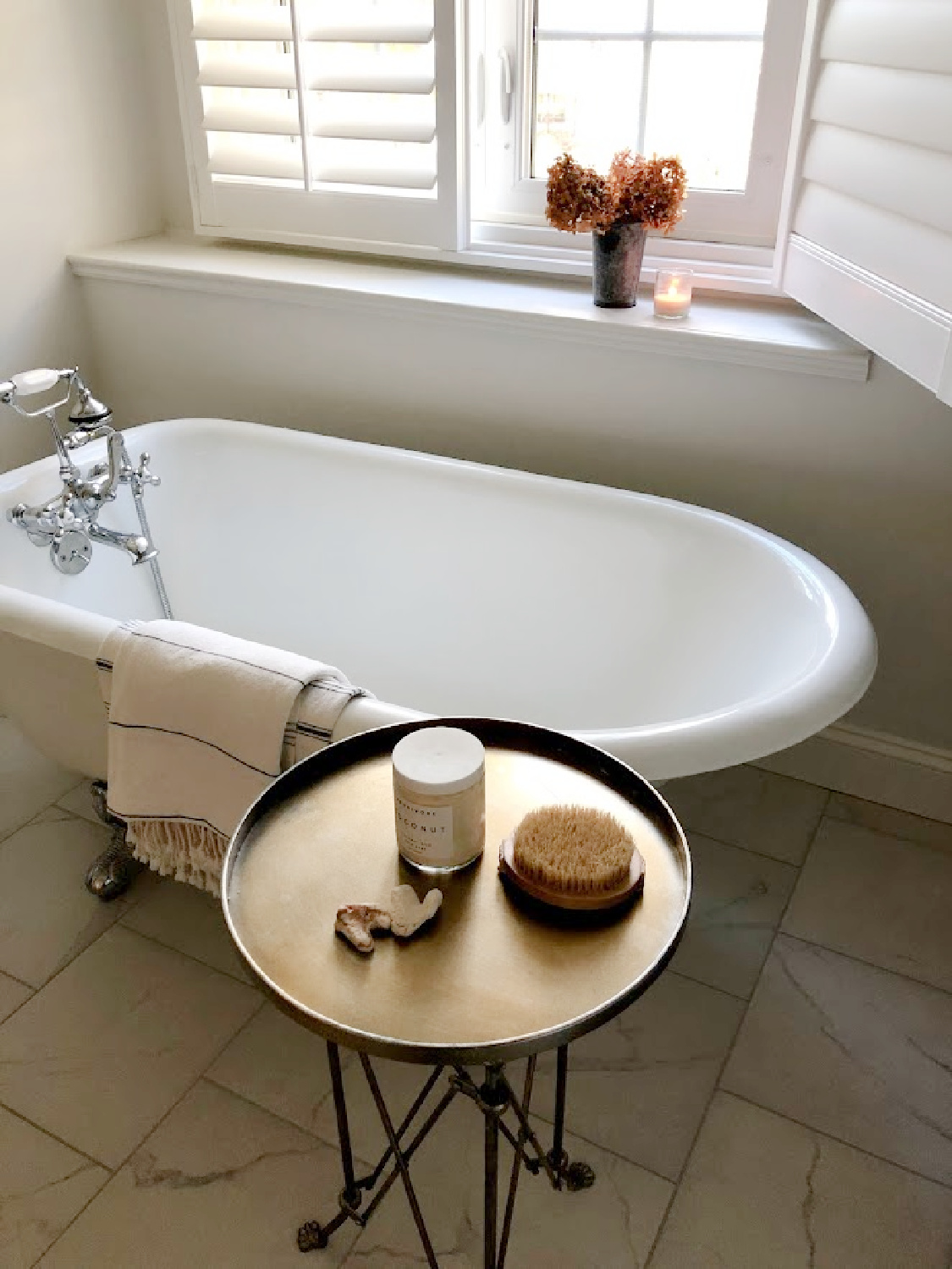 Vintage clawfoot tub in a serene white bath with plantation shutters - Hello Lovely Studio.