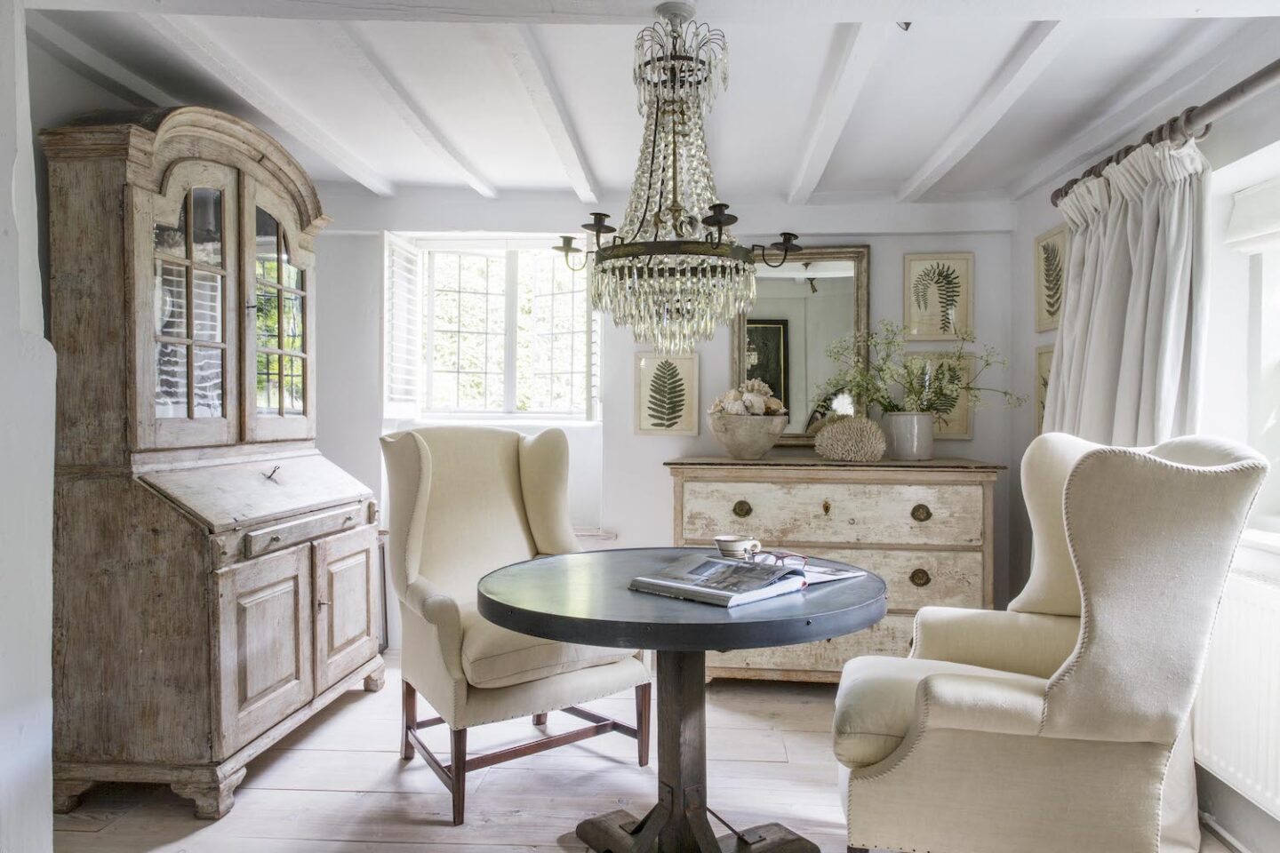 Wing chairs, European antiques, and crystal empire chandelier in a rustic 17th century English cottage - Anton & K.