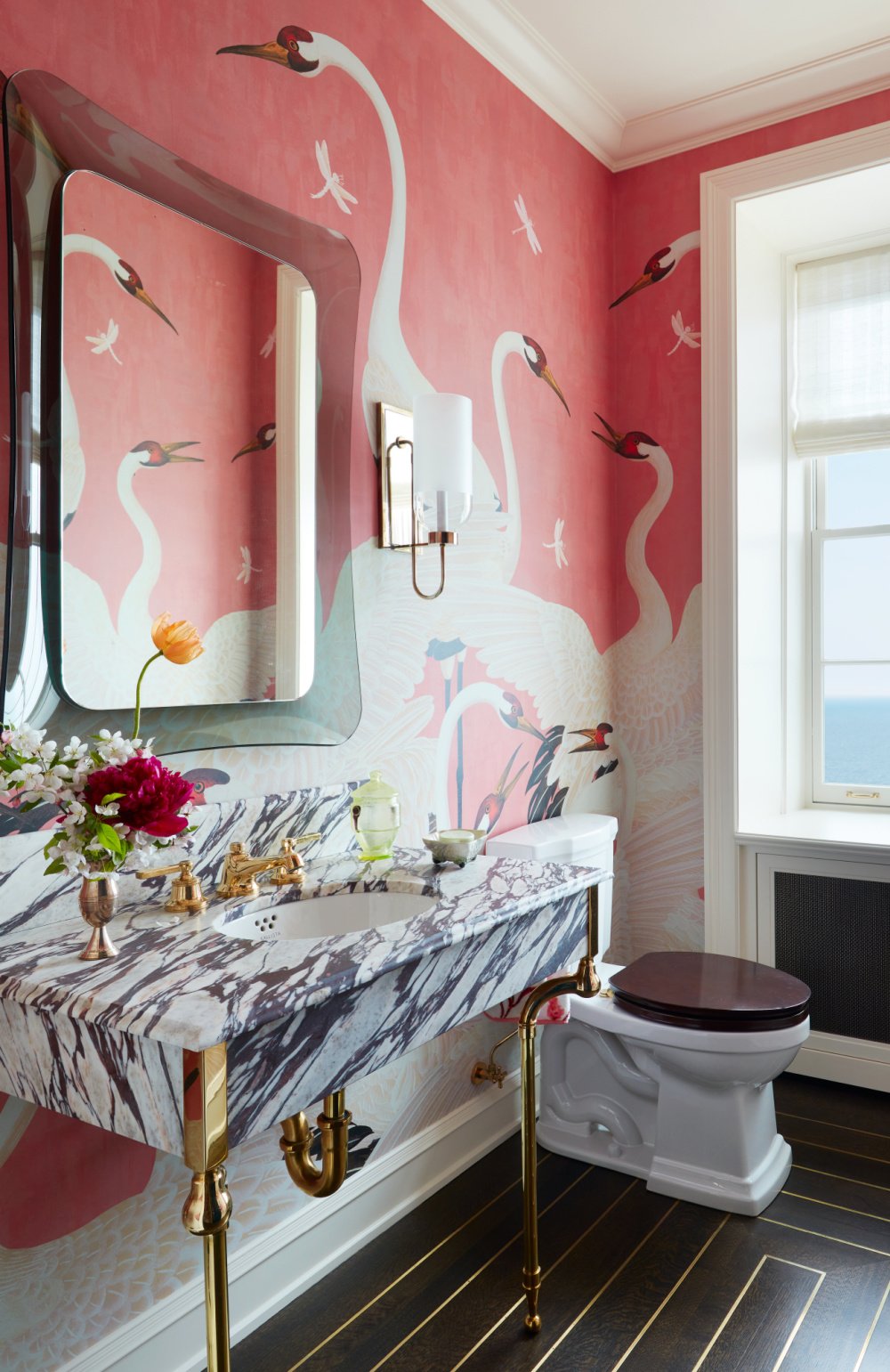 Summer Thornton designed bathroom wallpapered with whimsical giant white cranes on a hot pink background. Luxurious marble console sink and FontanaArte mirror. From WONDERLAND: Adventures in Decorating (Rizzoli, 2022). #summerthornton