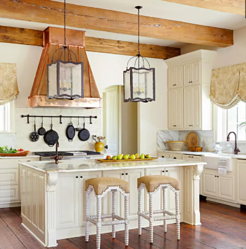 Copper range hood in a romantic French country kitchen with wood beams on ceiling and farm sink - BHG.