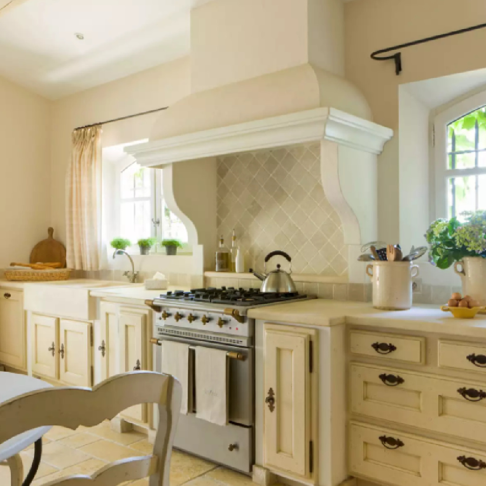 Arched windows flank the luxury range in a beautiful French country kitchen with farm sink - BHG.