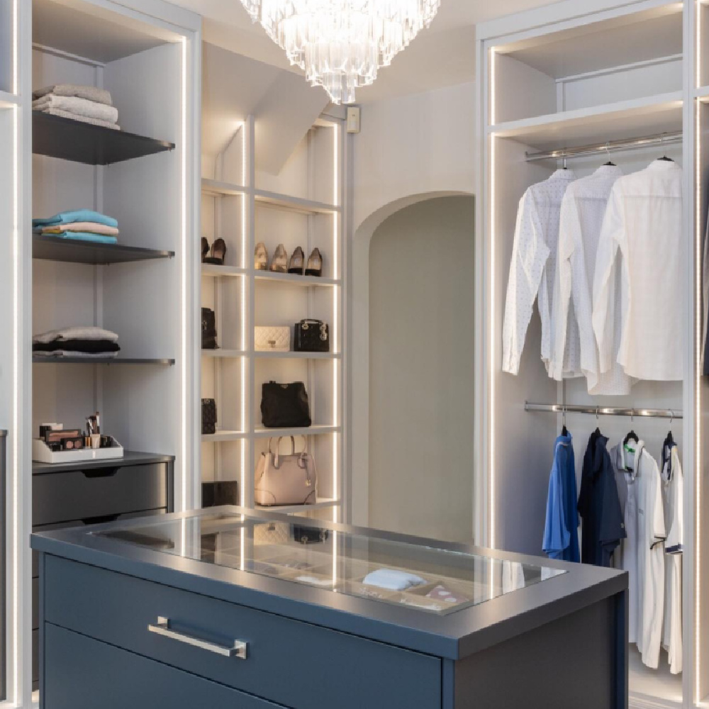 Beautiful custom closet with window, chandelier, island, and bespoke details - @johnlewisofhungerford. #customcloset #luxurycloset #dressingrooms